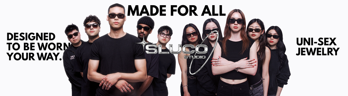 A group of nine models wearing black sunglasses and black clothing, standing against a white background with promotional text reading 'MADE FOR ALL', 'DESIGNED TO BE WORN YOUR WAY.', and 'UNI-SEX JEWELRY.